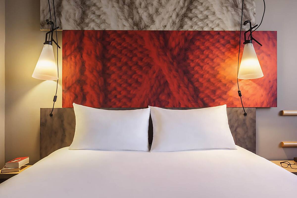 A hotel room with a bed, two bedside lamps, a marble headboard, and a red abstract painting on the wall.