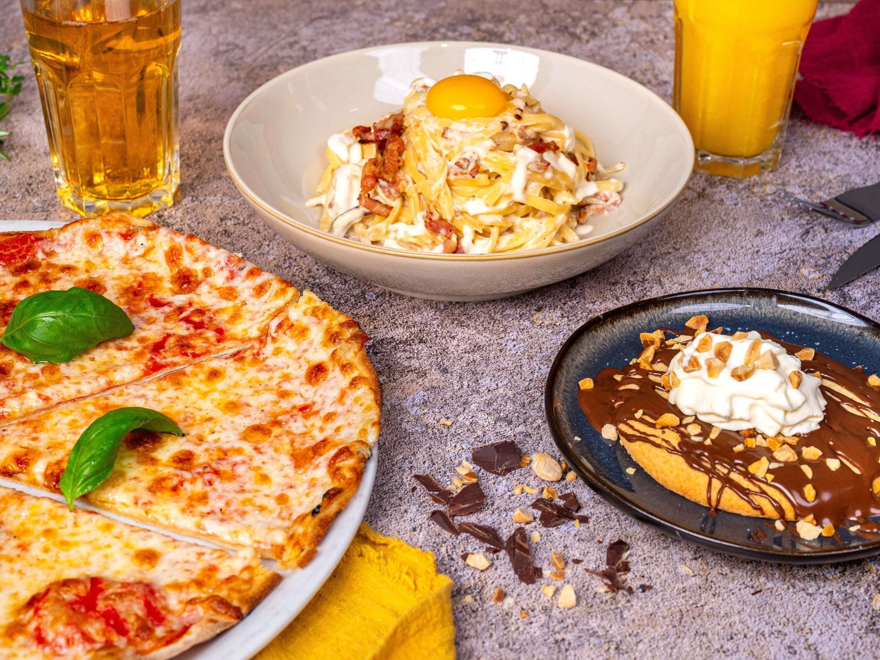 A pizza, a bowl of pasta, and a dessert plate with whipped cream and chocolate.