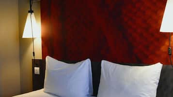 A hotel room with a bed, two white pillows, a red textured wall, and two wall-mounted lamps.