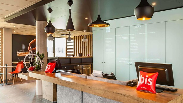 Een receptiebalie met een modern design, een digitaal scherm en een rode 'bis Hotels' tas.