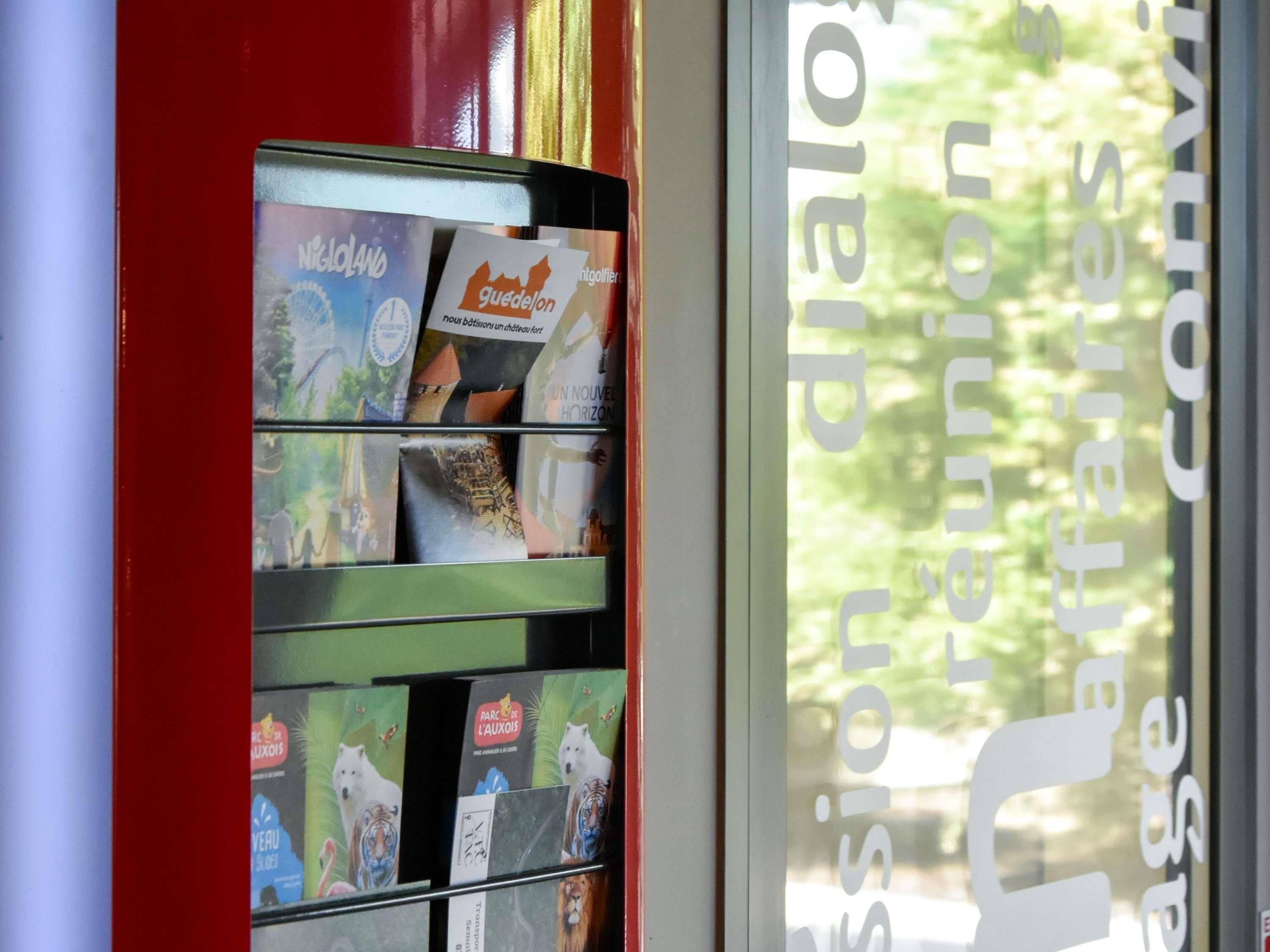 A vending machine with various travel brochures and a window with a view of greenery.