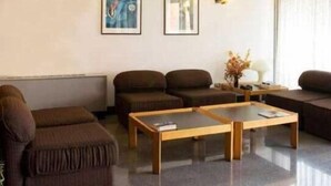 Een moderne woonkamer met een glazen salontafel, donkerbruine banken en twee kunstwerken in lijsten aan de muur.