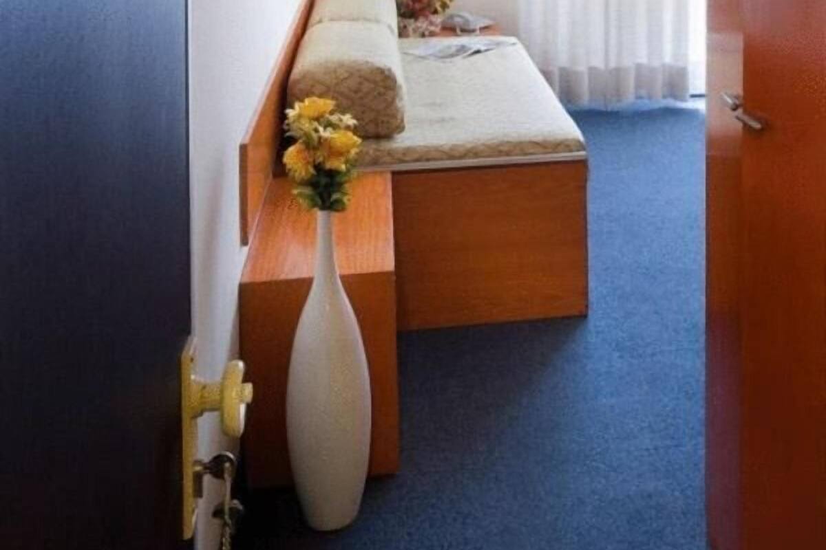 Un dormitorio con cama, mesita de noche, un jarrón con flores y una puerta.