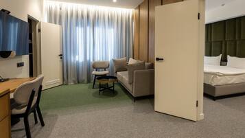 A hotel room with a bed, a sofa, a desk with a chair, and a small table with a chair.