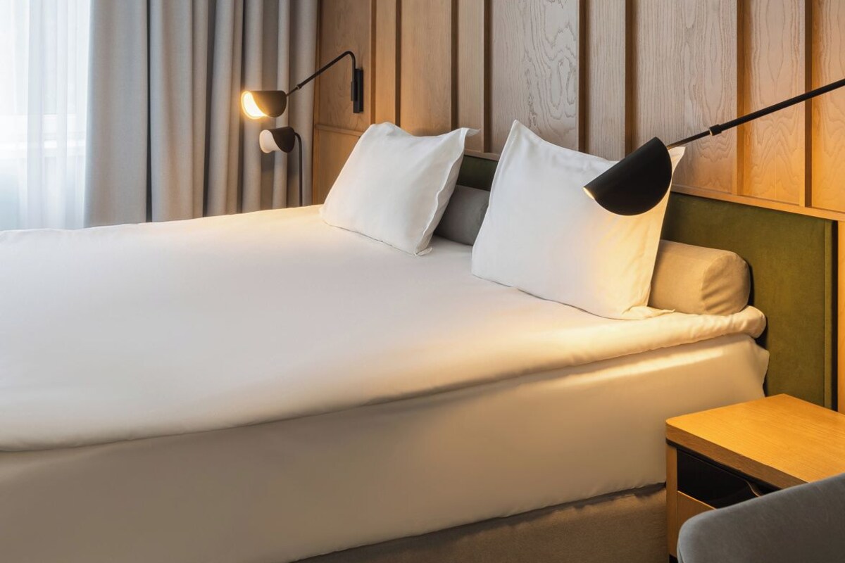 A hotel room with a large bed, two bedside lamps, and a wooden panel wall.