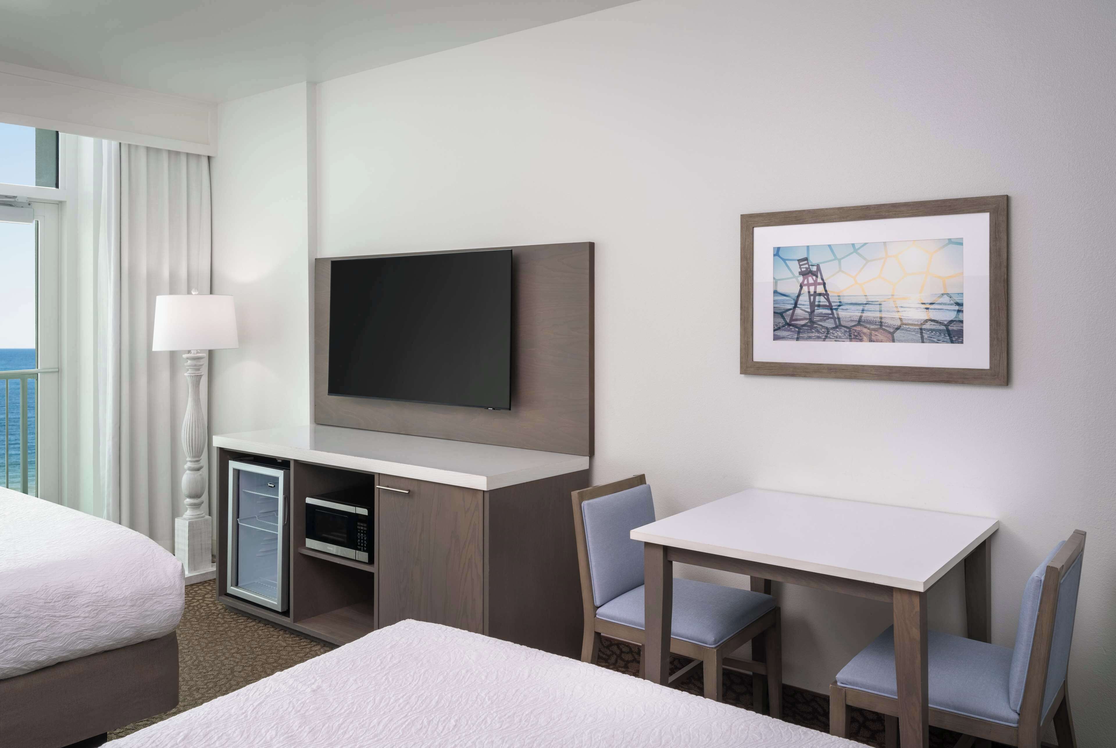Une chambre d’hôtel comprenant un lit, un bureau avec deux chaises, une télévision, un four à micro-ondes et un tableau encadré au mur.