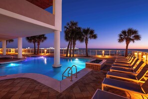 A swimming pool with lounge chairs and palm trees, surrounded by a white railing and a view of the ocean. - Best Western Premier The Tides (Orange Beach)