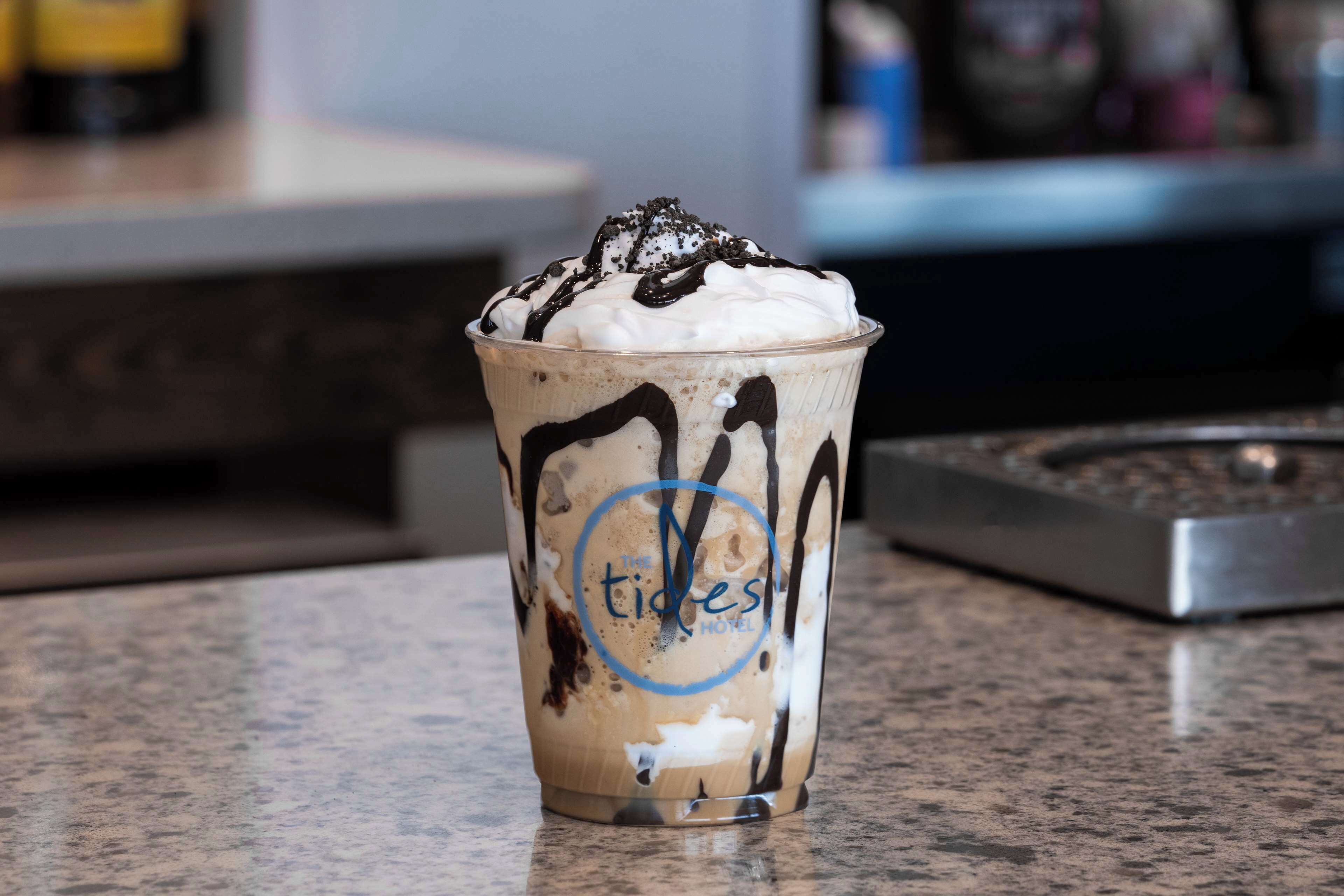 Una taza de café helado con crema batida y jarabe de chocolate sobre una encimera.
