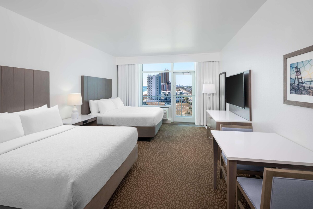 Habitación de hotel con dos camas, televisión, escritorio y vistas a la ciudad.