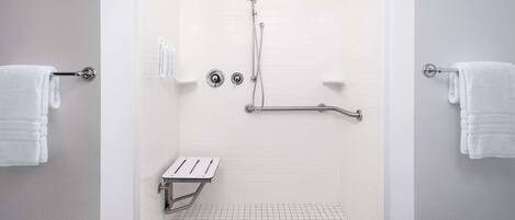 Un área de ducha moderna con puerta de cristal, paredes de azulejos blancos y una barra de apoyo de metal.