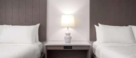 A hotel room with two beds, a bedside table with a lamp, and a control panel.