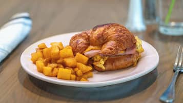 A plate with a croissant sandwich and cubed potatoes.