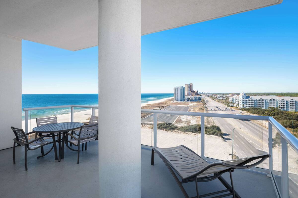 Un balcón con mesa y sillas, con vistas a la playa y al paisaje urbano.