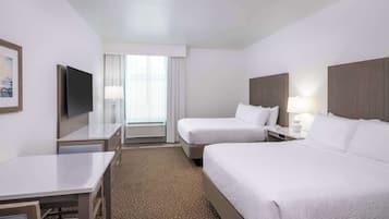 A hotel room with two beds, a desk, a TV, and a window with curtains.