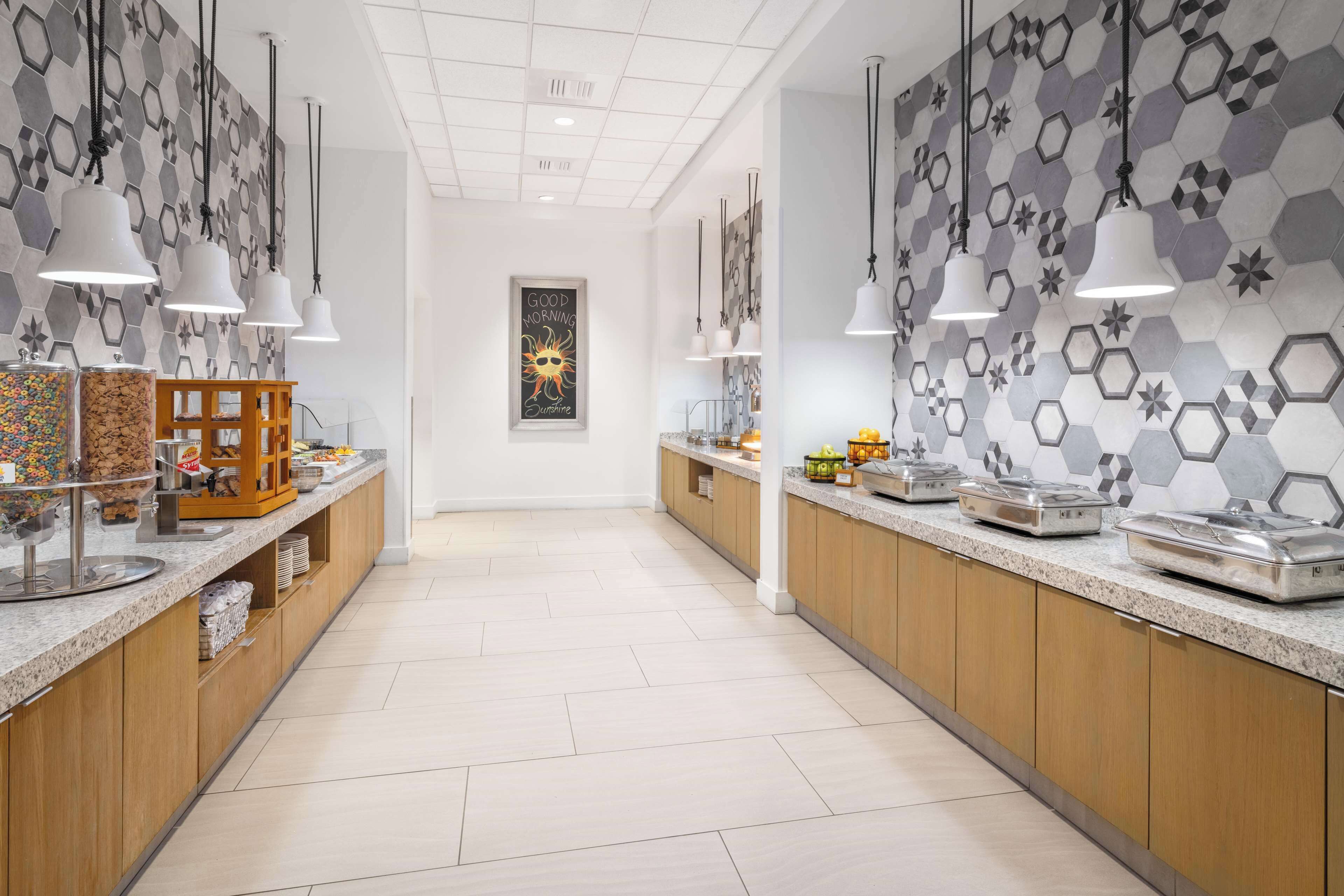 A modern kitchen with hexagonal tile walls, pendant lighting, and a central island with a wooden base.