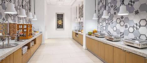 A modern kitchen with hexagonal tile walls, pendant lighting, and a central island with a wooden base.