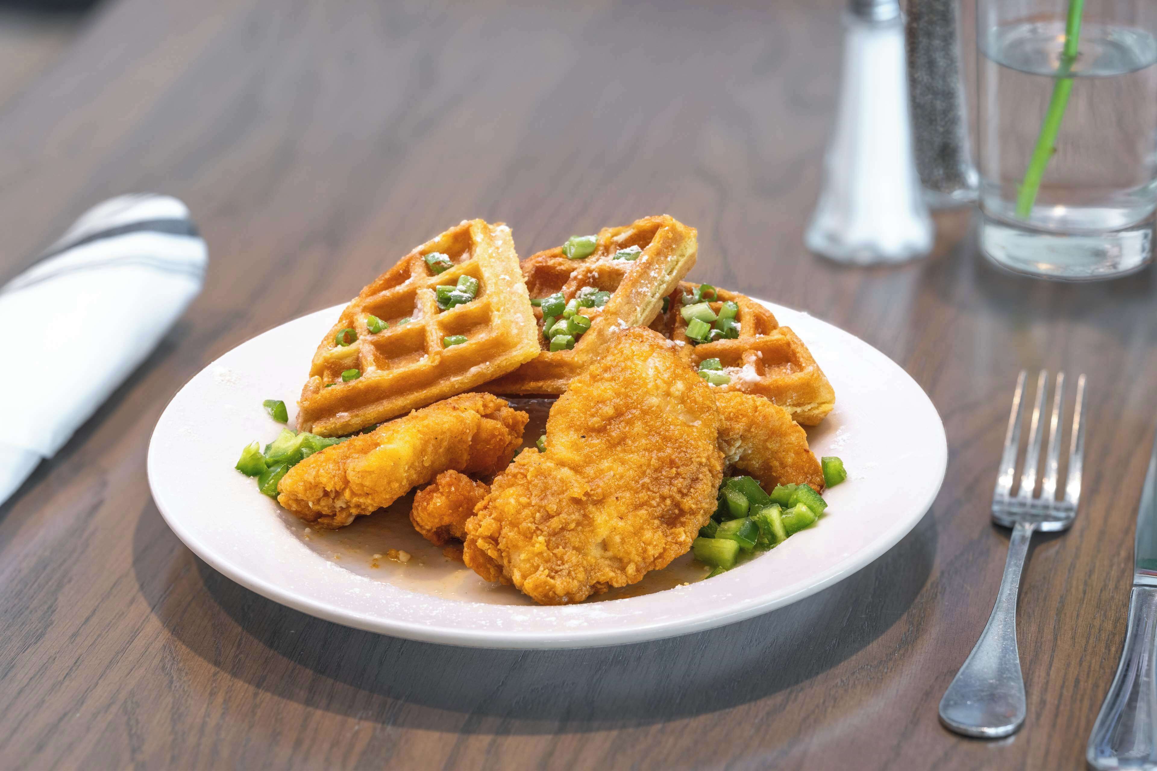Ein Teller Essen mit Waffeln und gebratenem Hähnchen auf einem Holztisch.