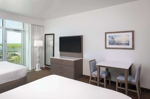 A hotel room with a bed, a desk with two chairs, a television, a dresser, and a window with curtains.