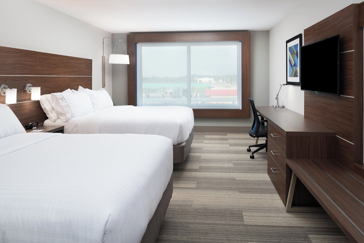 A hotel room with two beds, a desk, a chair, a TV, and a large window.