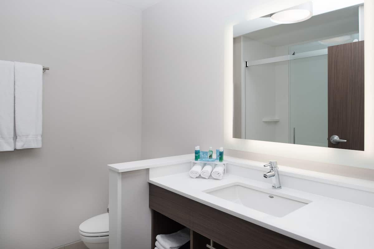 Un baño moderno con un lavabo blanco, un espejo grande y un perchero para toallas.