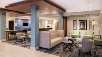 A hotel lobby with a seating area, a dining table, and a television.
