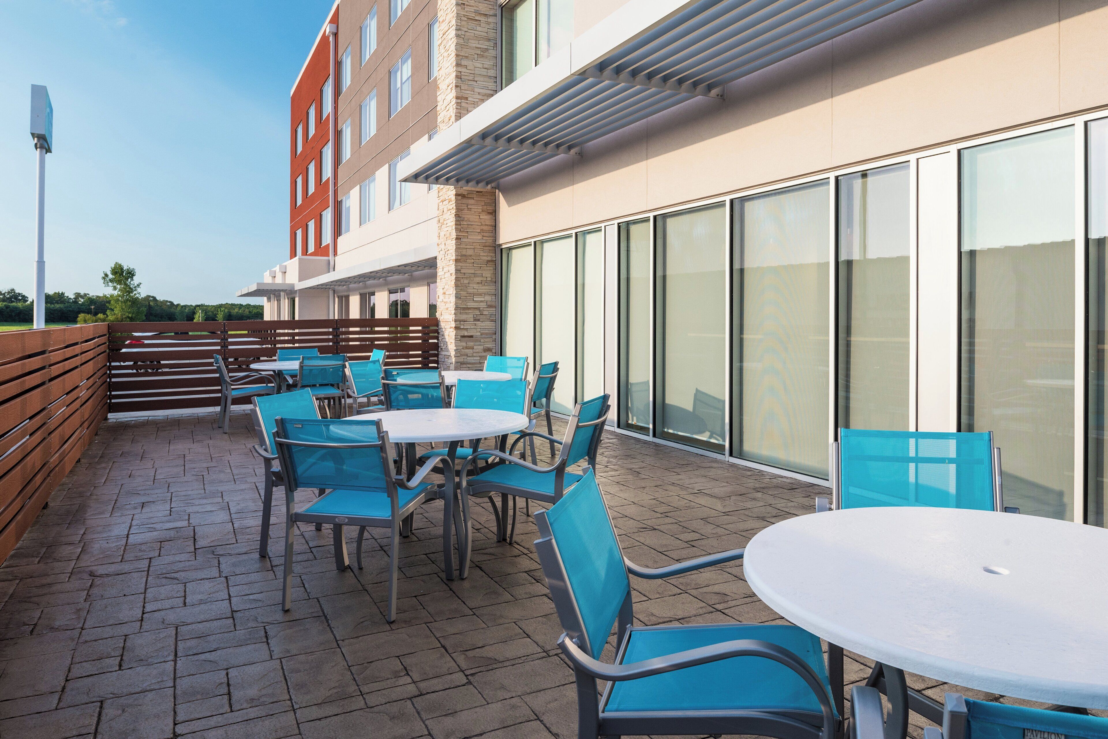 An outdoor seating area with tables and chairs, a stone wall, and a building with large windows.