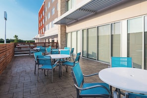 An outdoor seating area with tables and chairs, a stone wall, and a building with large windows. - Holiday Inn Express & Suites Kingdom City by IHG (Kingdom City)