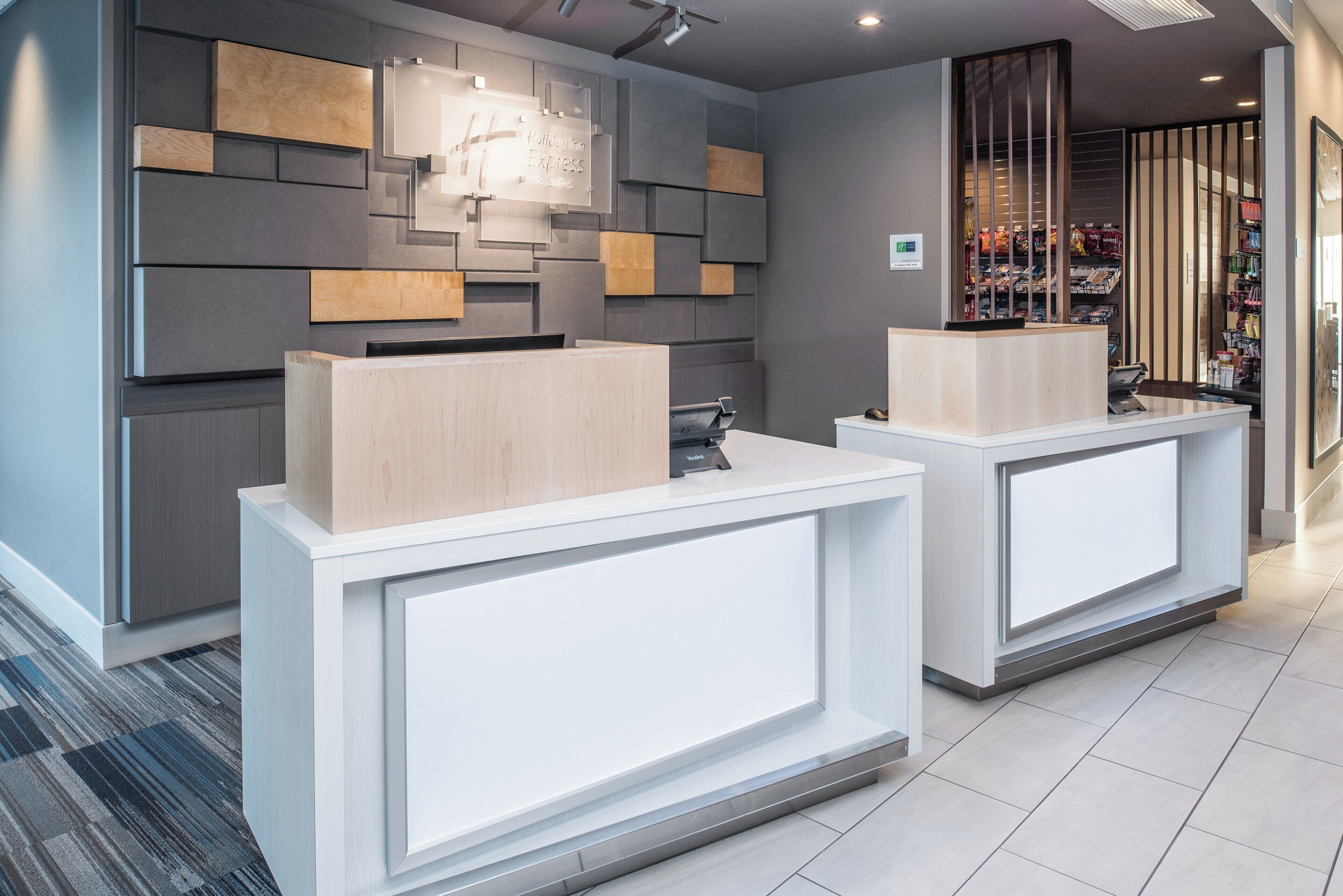 Ein Hotel-Rezeptionsbereich mit modernem Design, der zwei Empfangstische, eine Wandtafel und eine Auswahl an Snacks zeigt.