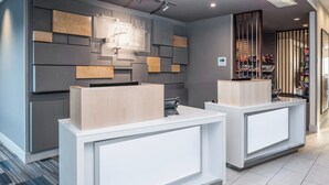 A hotel reception area with modern design, featuring two reception desks, a wall-mounted sign, and a display of snacks.