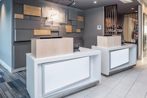 A hotel reception area with modern design, featuring two reception desks, a wall-mounted sign, and a display of snacks. - Holiday Inn Express & Suites Kingdom City by IHG (Kingdom City)