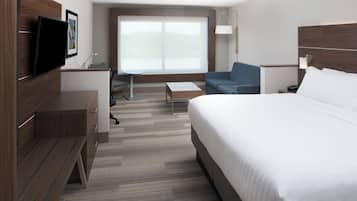 A modern hotel room with a large bed, a desk, a chair, a TV, and a large window.