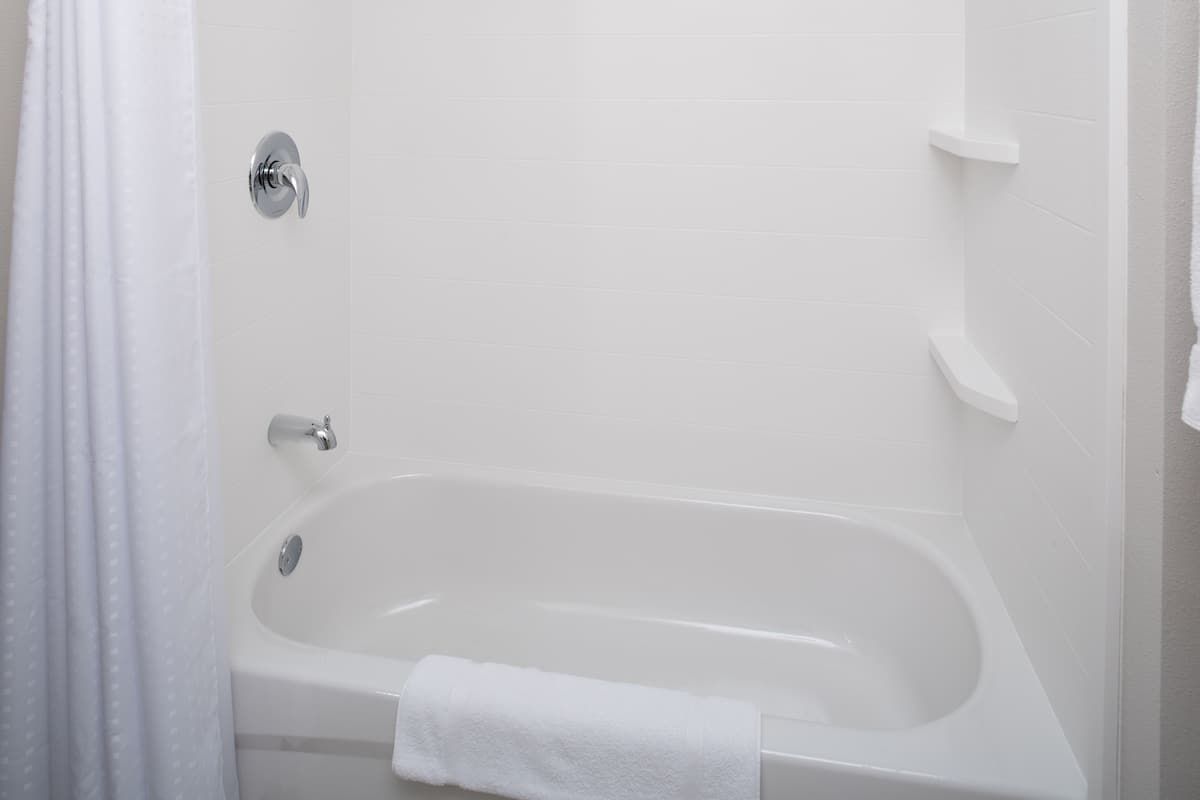 Un baño limpio y blanco con una bañera, una cortina de ducha y una toalla sobre la bañera.