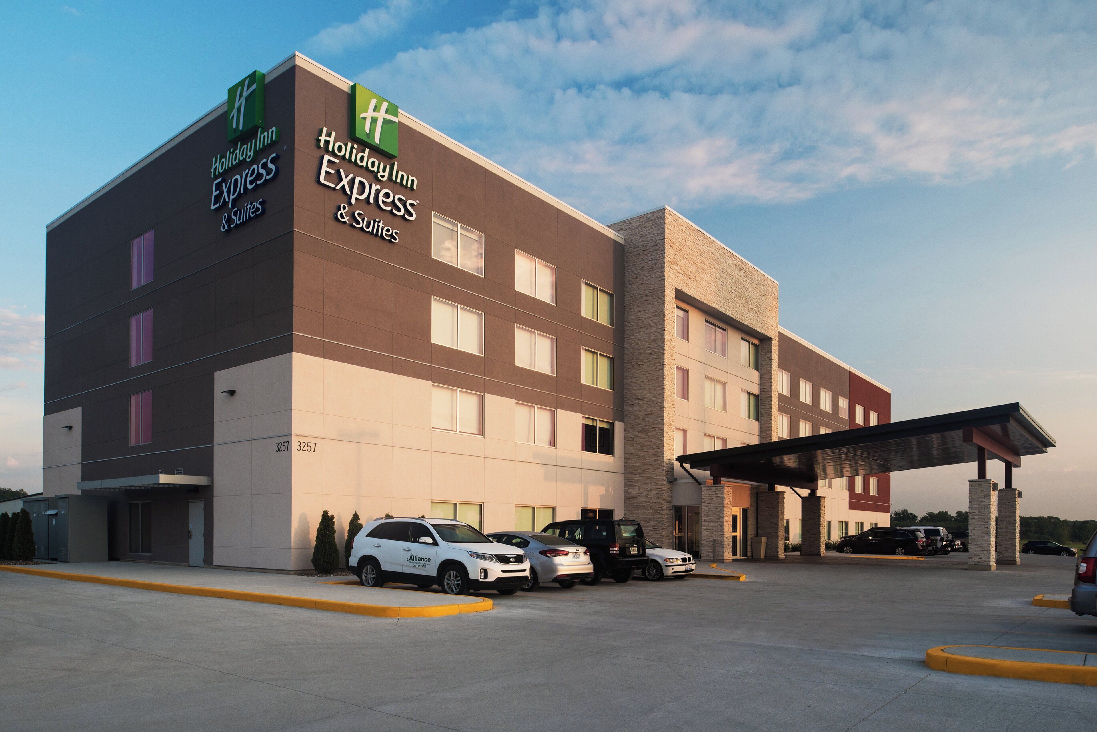 Un hotel Holiday Inn Express & Suites de diseño moderno, con un estacionamiento que muestra varios automóviles y una entrada cubierta.