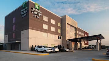 Un hotel Holiday Inn Express & Suites de diseño moderno, con un estacionamiento que muestra varios automóviles y una entrada cubierta.
