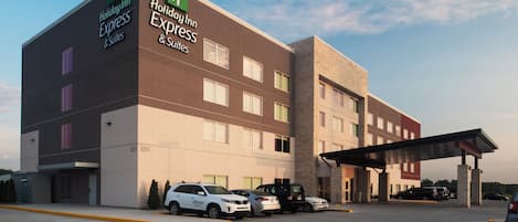 Un hotel Holiday Inn Express & Suites de diseño moderno, con un estacionamiento que muestra varios automóviles y una entrada cubierta.