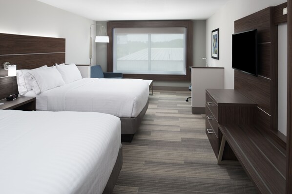 A hotel room with two beds, a TV, a desk, and a large window.