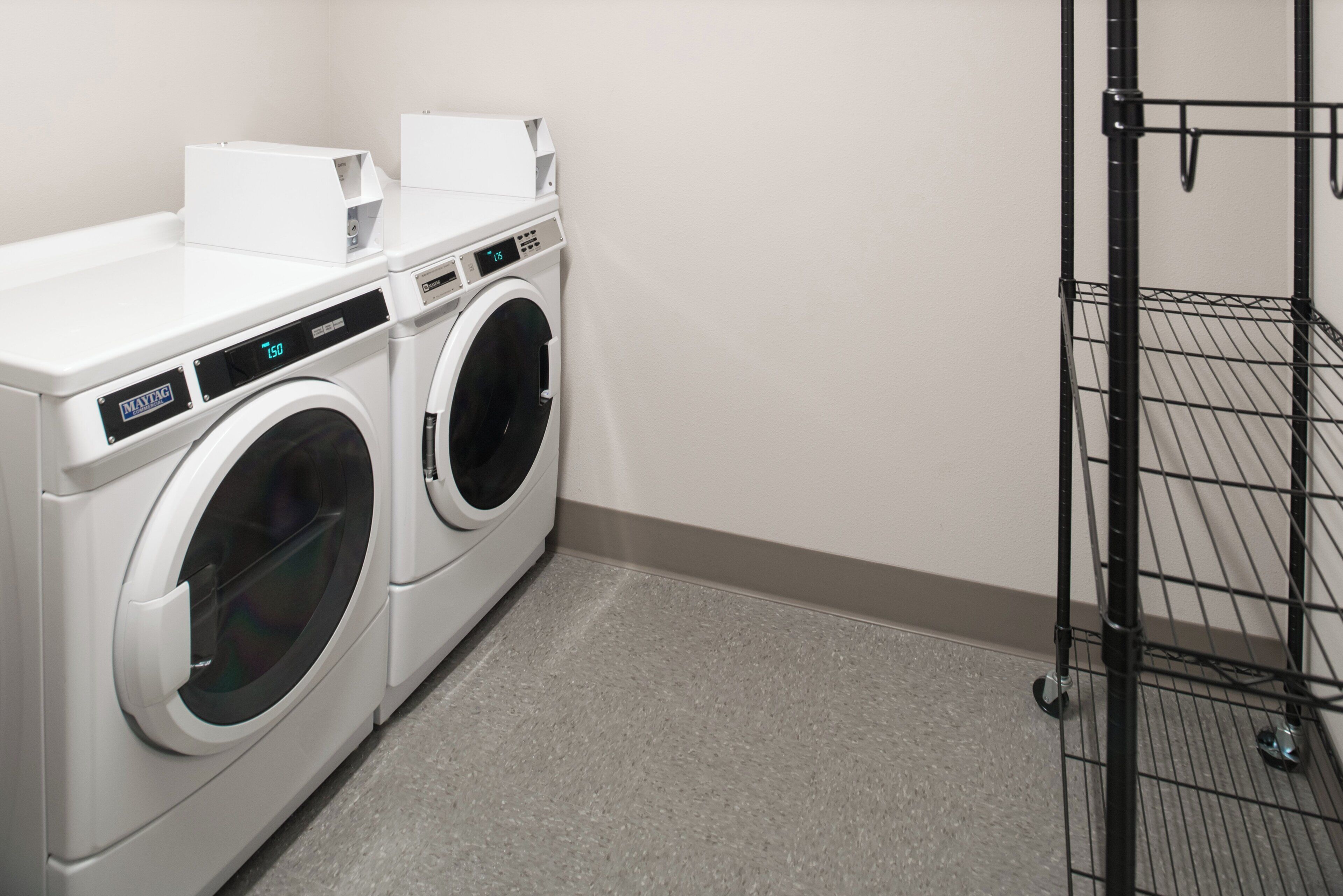 A laundry room with two front-loading washing machines and a metal drying rack.