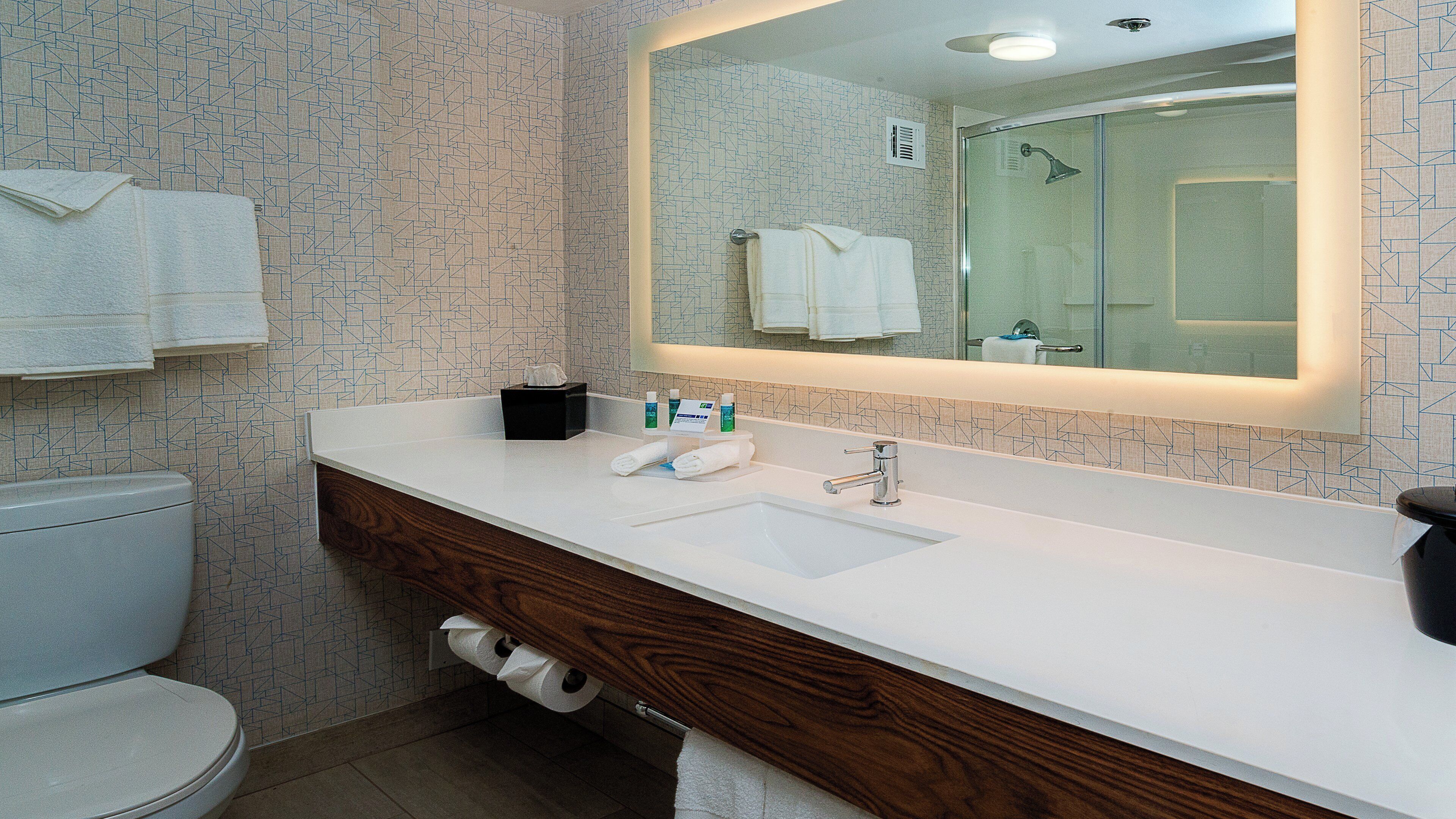 A bathroom with a white sink, wooden vanity, a mirror, and a toilet.