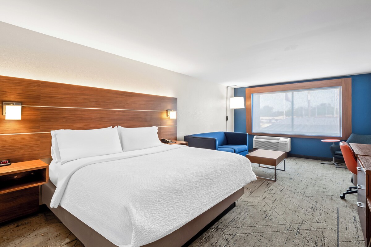 A hotel room with a large bed, a desk, a chair, and a window with a view.