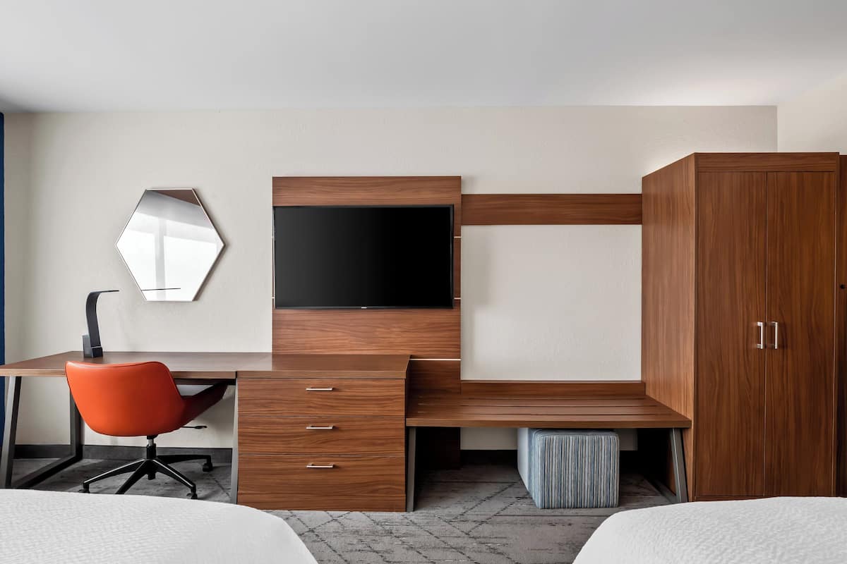 Habitación de hotel con un escritorio de madera, una silla moderna, un televisor de pantalla plana y un armario.