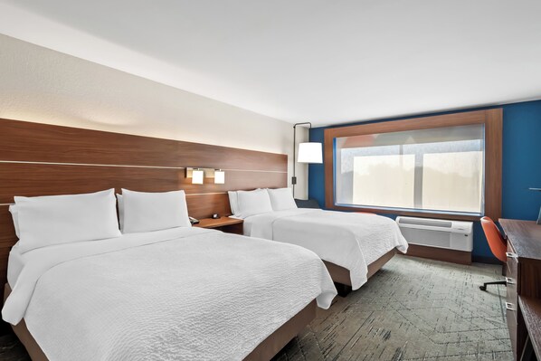 Une chambre d’hôtel avec deux lits, un bureau, une chaise, une fenêtre et un radiateur fixé au mur.