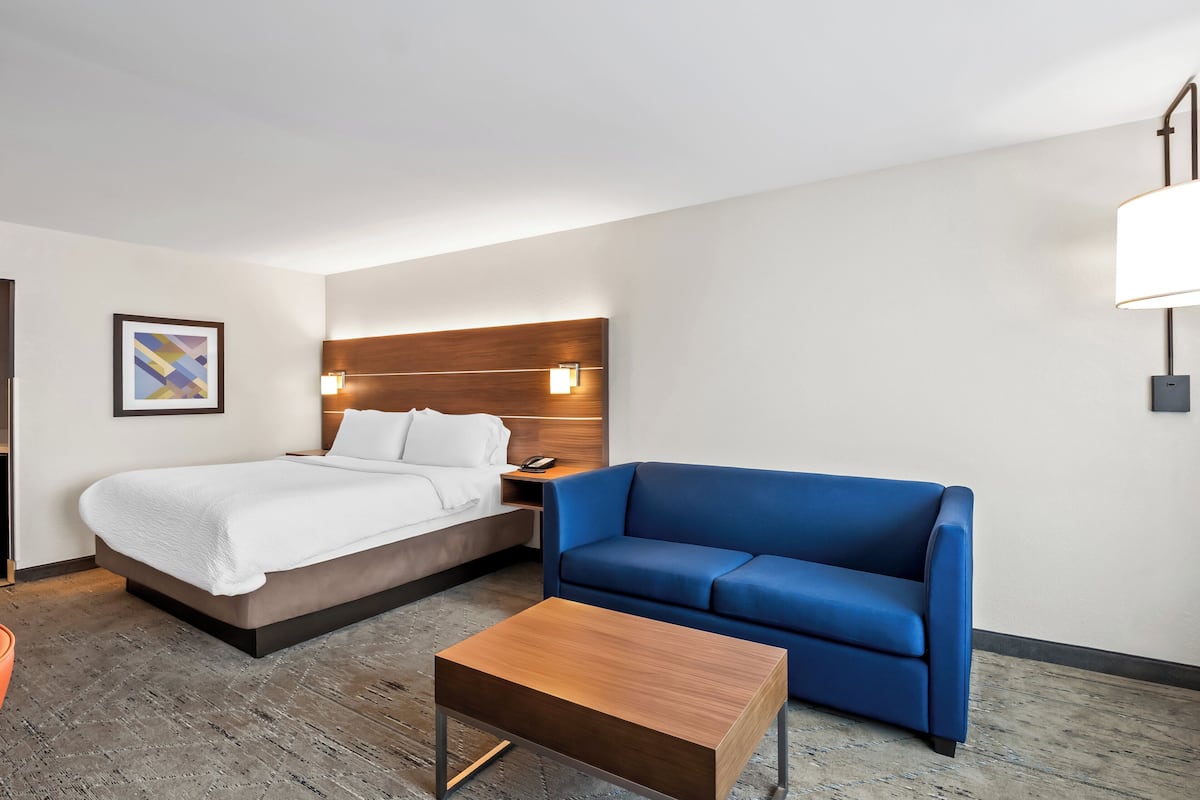 Una habitación de hotel con una cama, un sofá azul, una mesa de centro de madera y una mesita de noche con una lámpara.