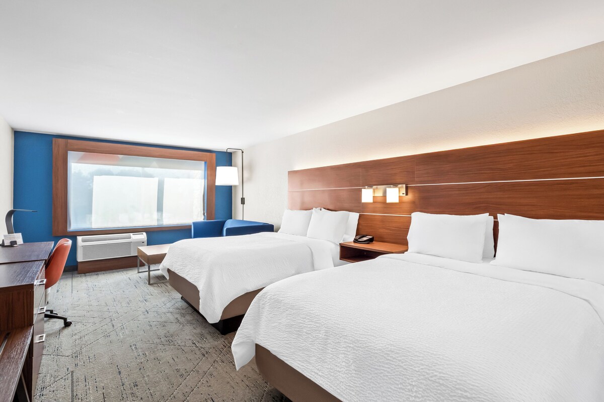A hotel room with two beds, a desk, a chair, and a window with blinds.