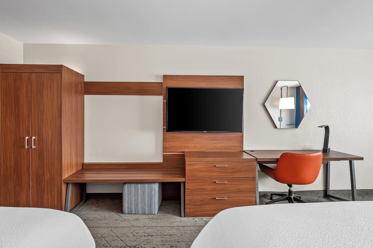 Habitación de hotel con un escritorio de madera, un televisor, un espejo y una silla naranja.
