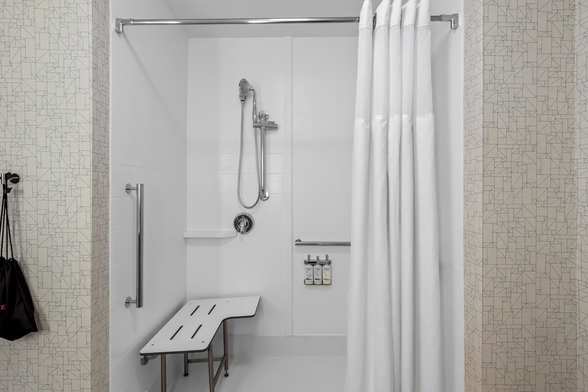 A modern shower area with a handheld showerhead, a towel bar, and a small bench.