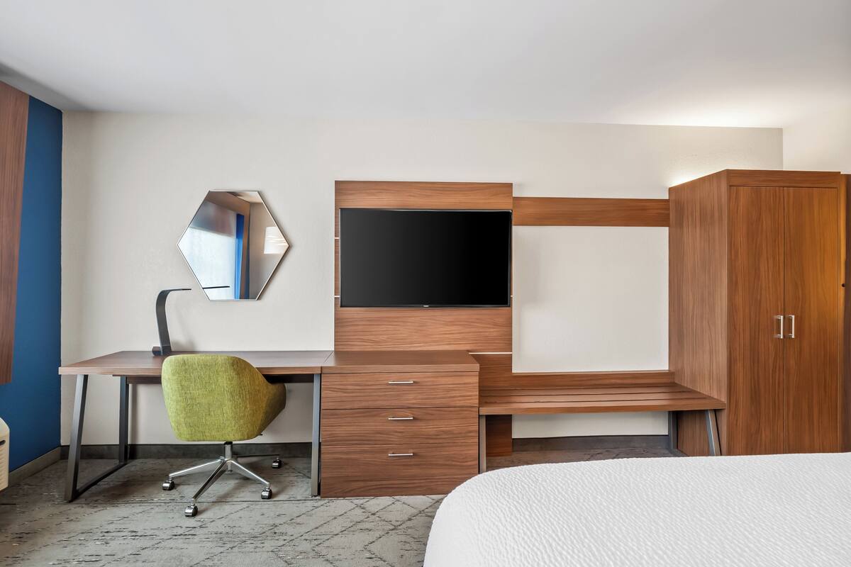 Habitación de hotel con escritorio de madera, silla de oficina verde, televisor de pantalla plana, armario y cama.
