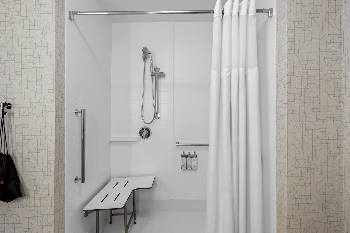 Un área de ducha moderna con cabezal de ducha de mano, una barra para toallas y un pequeño banco.