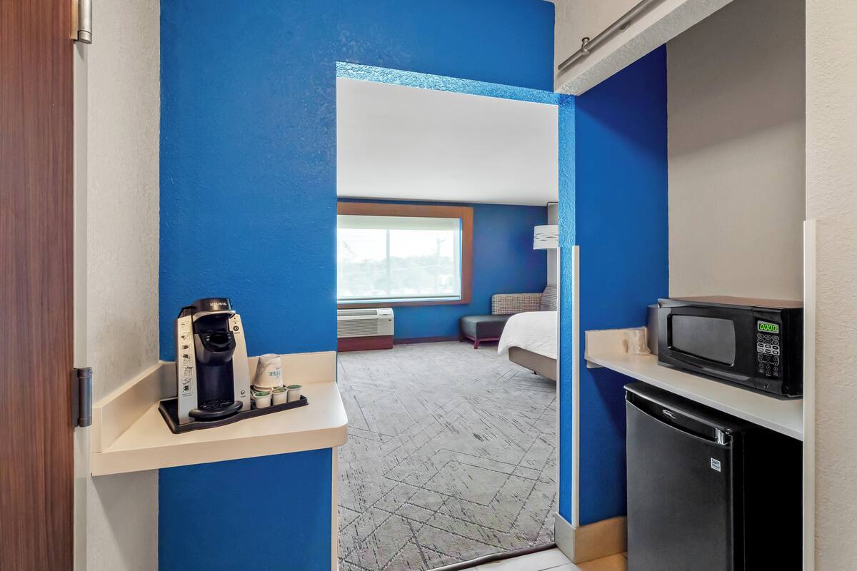 Una habitación de hotel compacta con kitchenette, una cama y una ventana.
