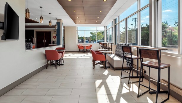A modern interior with a dining area, large windows, and a flat-screen TV. - Holiday Inn Express & Suites Detroit Northwest - Livonia by IHG (Livonia)