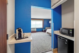 A compact hotel room with a kitchenette, a bed, and a window.